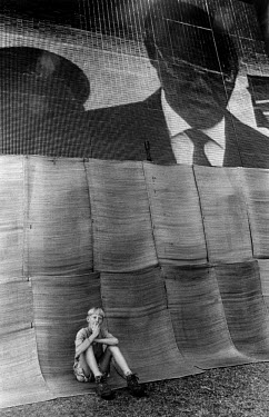 A boy sits beneath a big screen showing the inauguration of Nelson Mandela as President.