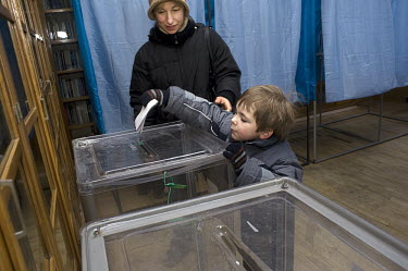 A child places a ballot into a voting box on behalf of his mother in the Shevchenko district of Kyiv during the first round of voting in the 2010 Presidential elections.