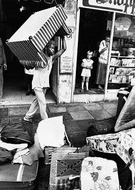 Black residents of Hillbrow are evicted from their apartment in the 'whites only' suburb. A white mother and child look on as an evicted tenant piles his furniture on the pavement. Under apartheid leg...