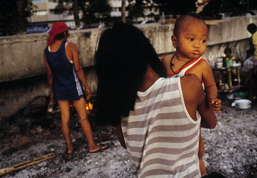 A woman carries her child on a beach where she lives. Several homeless families live on beaches in Manila, and children have to resort to begging on the streets.