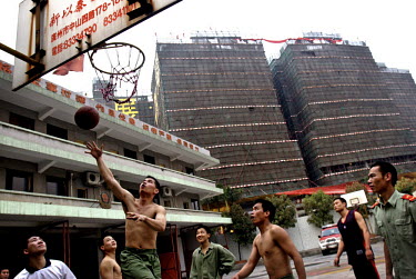Local fire fighters relax by playing basketball in the shadow of one of Guangzhou's massive construction projects.