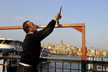 A man painting metalwork by an Eminonu ferry dock on the Golden Horn, with Galata across the water beyond.