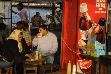 People eating fish sandwiches at a stall by the Golden Horn, next to advertising for Coca-Cola.