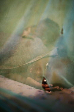 12 year old Eustella Ubisimgali in her bed at home under a mosquito net to protect her from malaria.