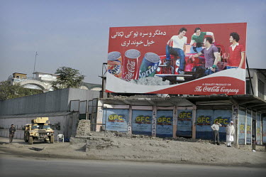 Security forces watch a street corner in Kabul. On the corner is a billboard advertising the Coca Cola Company, with images of cans of Fanta, Coca Cola and Sprite.