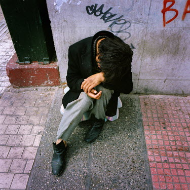 A homeless man begging on the pavement in front of Athens University.