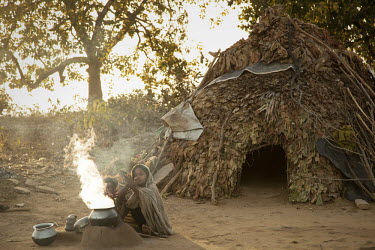 Two Birhor children warm themselves by an early morning fire in front of their leaf house. The Birhor Adivasi are the last remaining tribal group in Jharkhand who still attempt to live in their tradit...