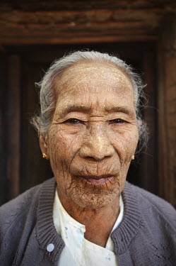 A portrait of a woman wearing tanaka, a natural sun-block made from the bark and wood of a tanaka tree. Her mouth is stained from chewing betel and areca nuts.