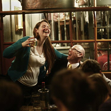 A man and a woman share a joke and a drink in a pub in the City of London.