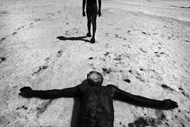 One man walks around in mineral rich black mud whilst another lies on the ground covered in the mud, to treat their skin at Lake Urmia, a salt lake in the province of West Azerbaijan. The salt and min...