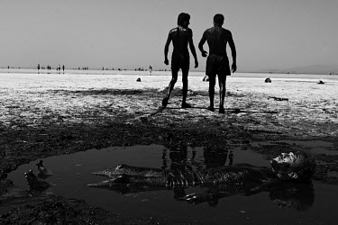 Men walk around in mineral rich black mud whilst another lies on the ground covered in the mud, to treat their skin at Lake Urmia, a salt lake in the province of West Azerbaijan. The salt and mineral...
