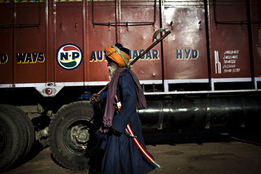 A man carrying a cresent axe walks past a truck at the Hola Mohalla Festival. It takes place on the first day of the lunar month of Chet (March/April).