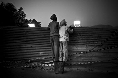 Two Sikh men stand on an old can in order to view the scene at night during the Hola Mohalla Festival. It takes place on the first day of the lunar month of Chet (March/April).