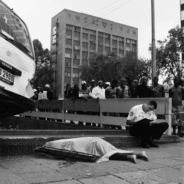 A crowd of people watch as a policeman writes a report about a road traffic accident at the junction of Rissik and Wolmarans Streets. The accident involved a taxi and there is a fatality lying on the...