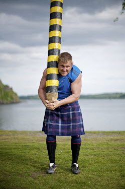 Neil Elliott wears a kilt and holds a caber near his home in Dumbarton. He competes in over 40 Highland Games and heavyweight events across the world throughout the summer.