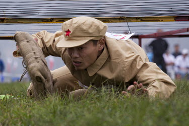 A competitor dressed in a PLA (People's Liberation Army) revolutionary era outfit crawls under 'barbed-wire' carrying a 'bomb' in the 'Storming the Enemy Blockhouse' event at the Red Games. Held in Ju...
