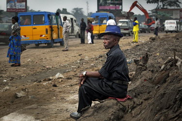 A sapeur watches traffic and roadworks on a road under construction in Kinshasa. Sapeurs here wear expensive clothing though live in poverty. The name comes from the SAPE (Societe des Ambianceurs et d...