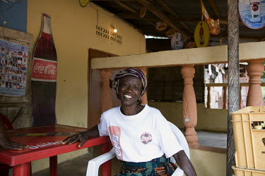 Mrs. Ejenwa sits at a table, wearing a Coca-Cola t-shirt, in the cafe that she runs in the town centre.