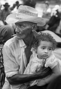 A farmer, with a child in his arms, waits for the departure of a boat carrying a group of people across the Gulf of Uraba to Cacarica. There they are to join with other returnees to found a 'Peace Com...
