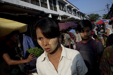Women wearing tanaka face powder walk through a Rangoon (Yangon) market. Tanaka powder comes from a plant and is said have various health benefits for the skin.