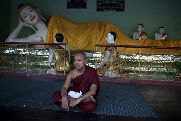 A monk sits in front of a reclining Buddha in the Shwedagon Pagoda.