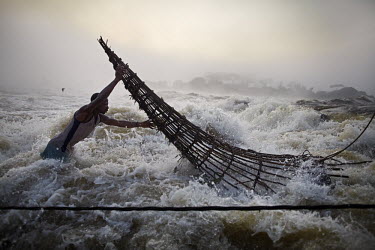 A fishermen, stands in a torrent of water as he checks a fish trap attached to a wooden scaffold at Boyoma Falls (known locally as Wagenia Falls). This is the last of seven cataracts below which the L...