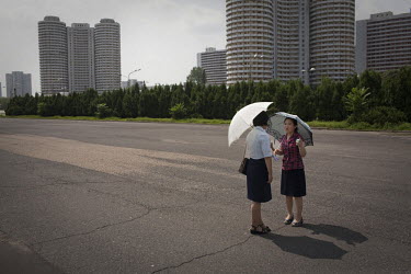 Two women talk under umbrellas on a deserted street near apartment buildings in Pyongyang.