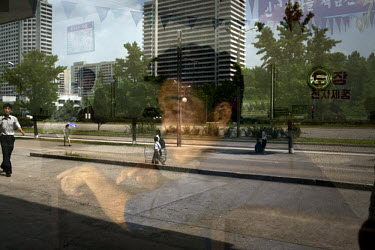 A man looks out of a window at a reflected street scene in Pyongyang.