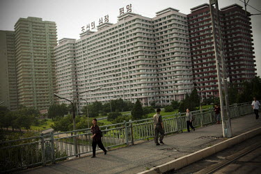People walk along a pavement on a bridge past apartment buildings in Pyongyang.