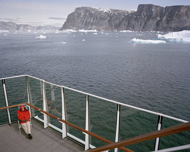 A woman sits on the deck of a luxury cruise liner as it passes through Uummannaq Bay.