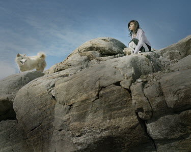 A girl on top of a rock with a husky dog.