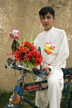 A young boy dressed in his best clothes sits on his bicycle elaborately decorated with plastic flowers.