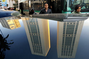 Pedestrians pass a parked car with the towers of the Casablanca Twin Centre reflected in its roof.