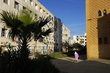 A woman walks past a mosque standing next to a housing block.