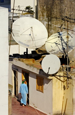 A woman walks into a rooftop room that supports three huge satellite dishes.