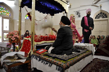 The wedding ceremony of British/Punjabi couple Lindsay and Navneet Singh at a gurdwara in Amritsar. The couple walk around the priest and Sikh holy book tied together with a pink scarf.