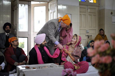 At the wedding ceremony of British/Punjabi couple Lindsay and Navneet Singh at a gurdwara in Amritsar, the bride's father attaches a pink scarf to the bride and groom.
