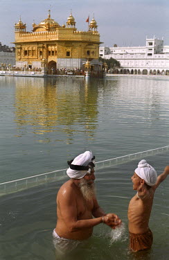 A young boy and his father bathe in the water tank that surrounds the Golden Temple at Amritsar, the holiest of all Sikh shrines.