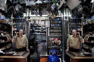 50 year old Omar Labbad sells gas heaters and accessories at a souk in Aleppo's old town. He talks on a mobile phone and is reflected in a glass mirror. Omar has been selling gas heaters since he was...
