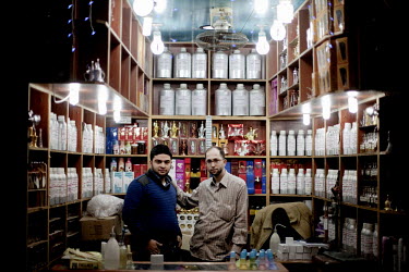 33 year old Bilal Seyrafi (right) and 18 year old Ibrahim Ashkar pose in their fake perfume shop which they have been running for five years at a souk in Aleppo's old town.