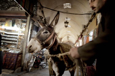 A man leads his donkey down an alley past shops at a souk in Aleppo's old town.