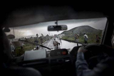 Viewed from a vehicle, men, women and children flee along the main road into Goma. They carry essential possessions like mattresses and blankets. Many go to refugee camps, others seek refuge with fami...