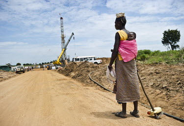 A woman carrying a child on her way to her field passes the entrance to Kigogole oil field, drilling site of Tullow Oil. As the site expands, the local population often have no other choice but to giv...