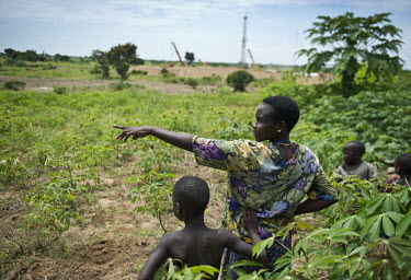 A mother with her children in a field of cassava plants. In the distance is the Kigogole oil field, drilling site of Tullow Oil. As the site expands, the local population often have no other choice th...