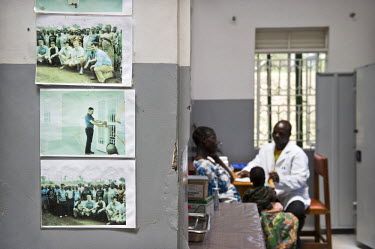 A doctor speaks to patients at a hospital. On the wall are photographs of the hospital's opening with executives from oil company Tullow Oil, who built the hospital and who drill nearby at Kigogole oi...