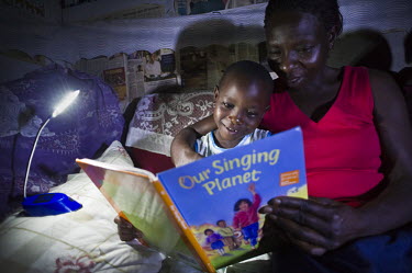 Christine Akurut, a primary school teacher, reads a bedtime book to her children, using the light of the Firefly, a portable LED lamp powered by solar energy.