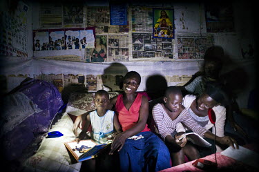 Christine Akurut, a primary school teacher, reads a bedtime book to her children, using the light of the Firefly, a portable LED lamp powered by solar energy.