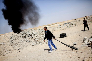 A rebel fighter drags a gun along the ground next to a burning military vehicle emitting black smoke following an intense battle between pro and anti Gadaffi forces near the town of Ajdabiya. On 17 Fe...