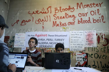 Local journalists discuss and update the Facebook page of the 17 February Movement, as the revolutionary movement is sometimes dubbed. Graffiti on the wall reads 'Bloody Monster stealing our oil, make...
