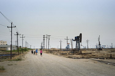 A family walks past a field of oil derricks near Bibi Heybat.